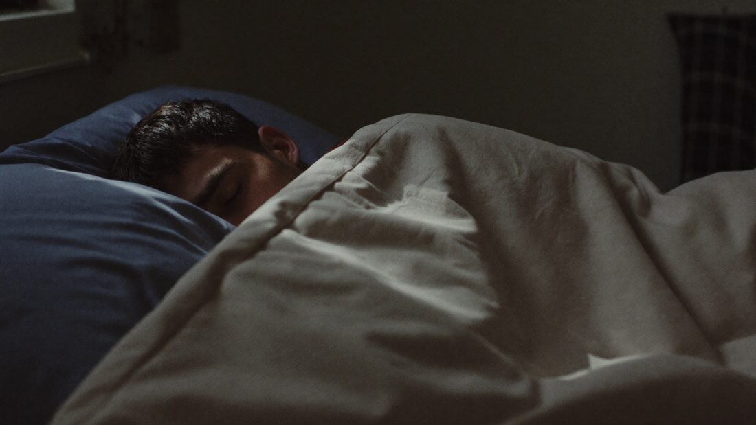 Man in his forties sleeping on his side in a dark bedroom, with soft moonlight over the duvet
