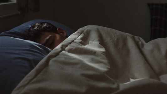 Man in his forties sleeping on his side in a dark bedroom, with soft moonlight over the duvet