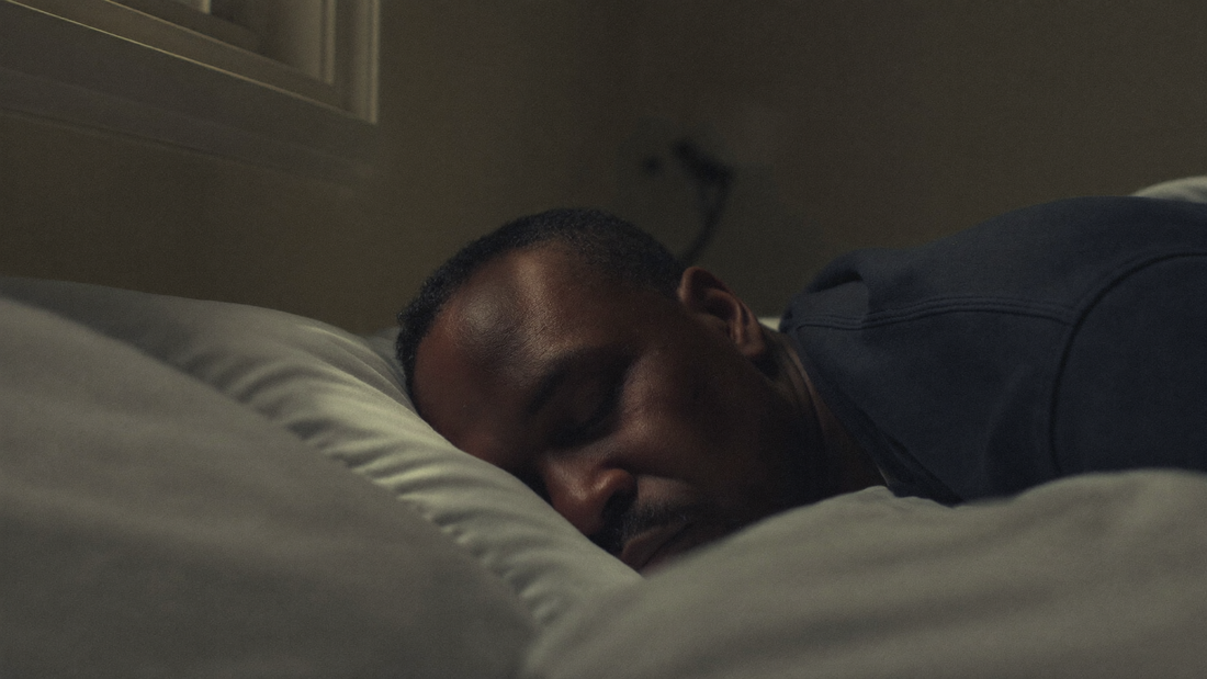 A man is sleeping on his side in a dark bedroom, with soft moonlight on his face and nose