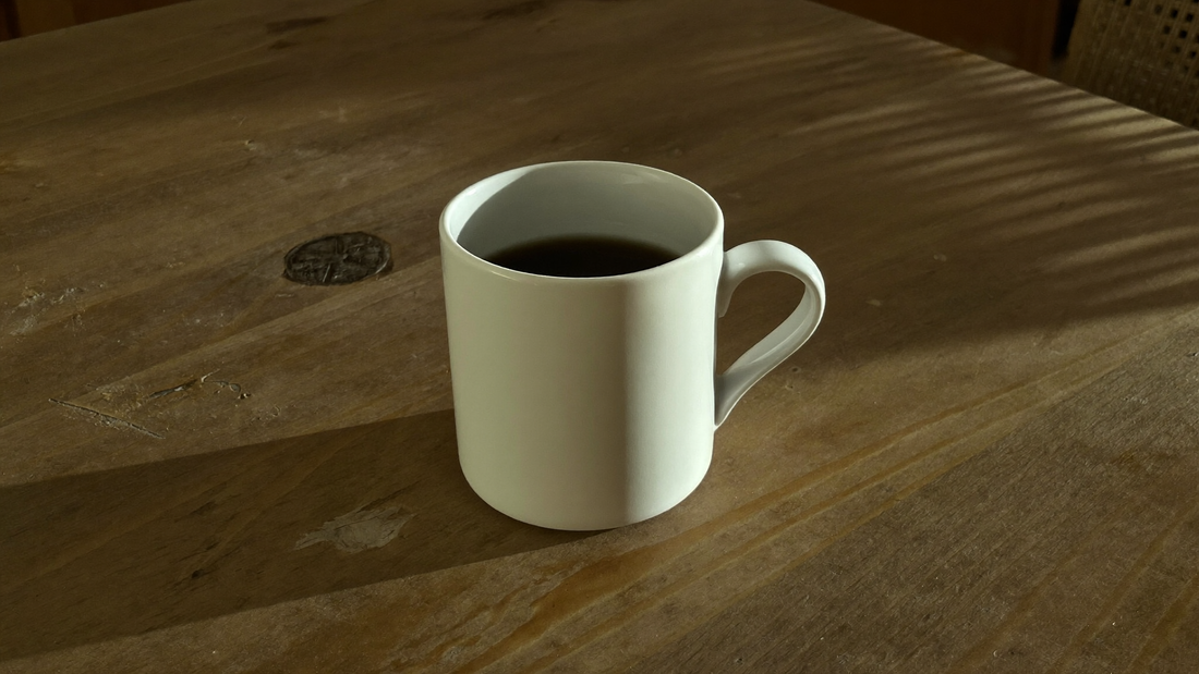 White cup of black coffee on a wooden table in the late afternoon light