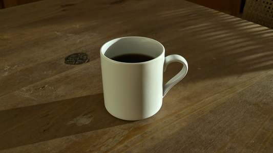 White cup of black coffee on a wooden table in the late afternoon light