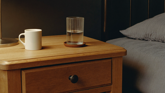 Nachtkastje met een glas water en een mok in het licht van een schemerlamp