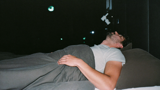 Man ligt op zijn rug wakker in bed in een donkere slaapkamer met het dekbed tot zijn borst